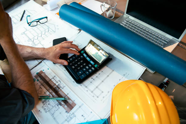 Unrecognizable Architect calculating and working on project at his work desk. Cut out image of male hands using calculator on the blueprint drawing